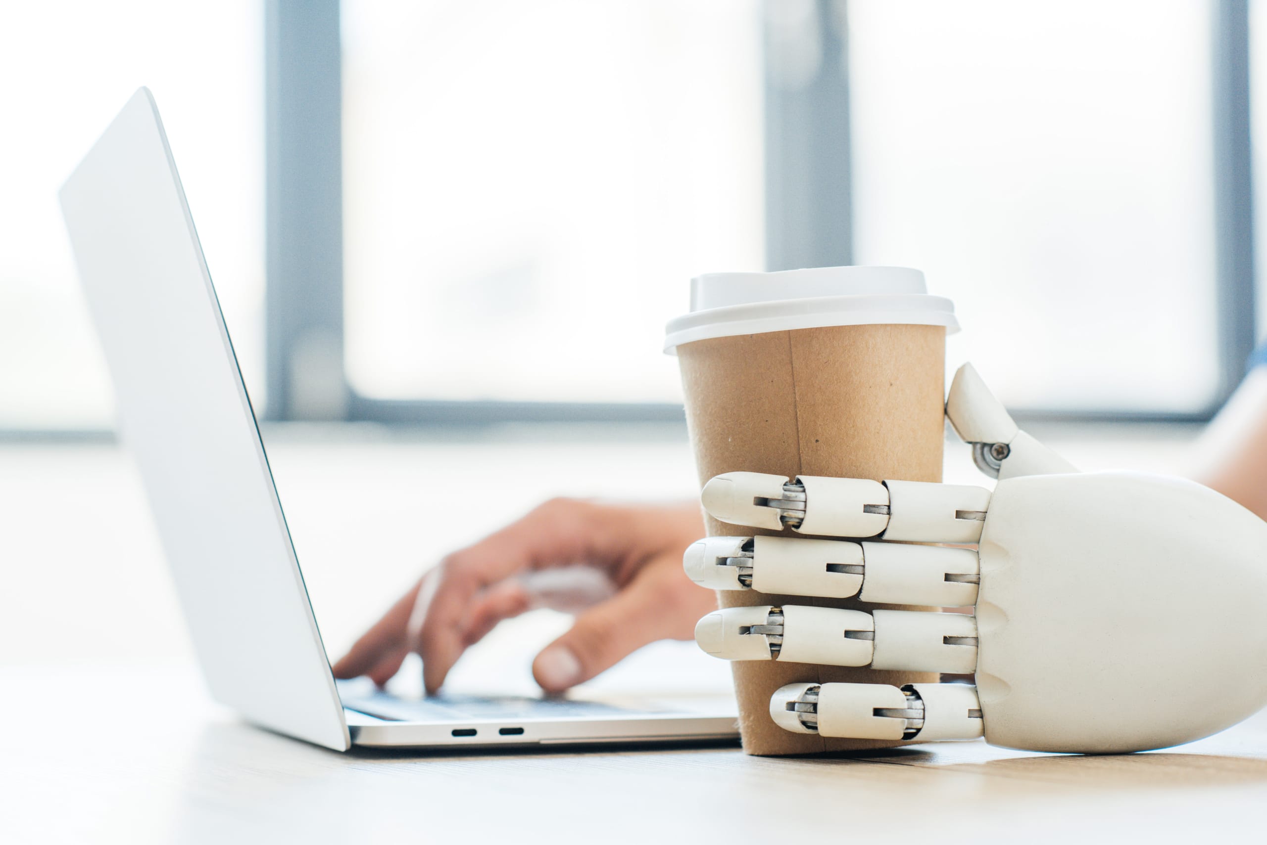 close-up view of robotic arm holding disposable coffee cup and human hand using laptop un chatbot peut devenir un véritable prolongement de votre service client plutôt qu’un simple gadget technologique.