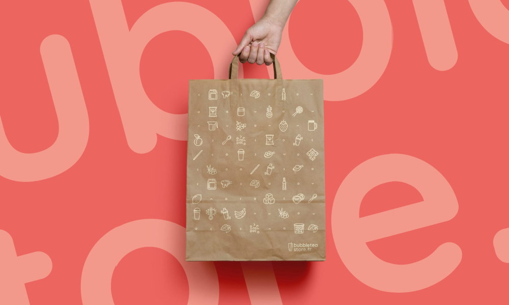 Sac en papier de bubble tea avec des illustrations, tenu par une main.