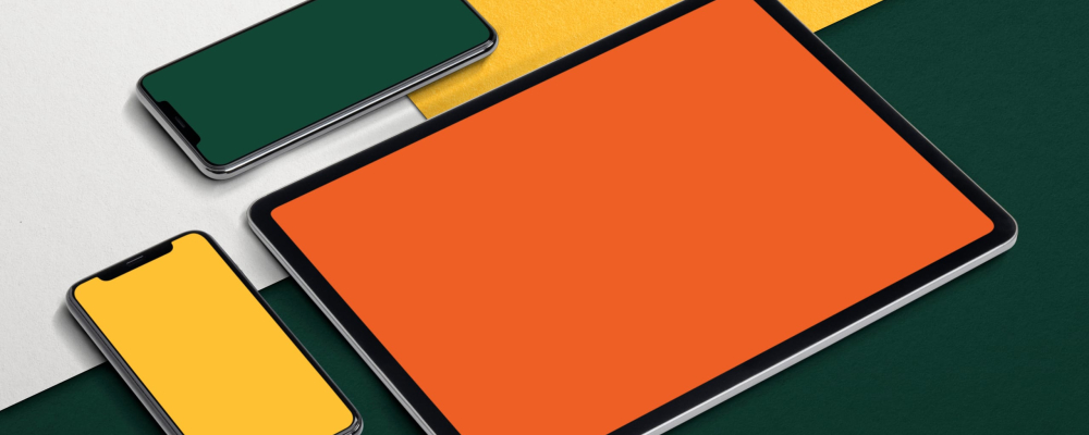 Une tablette et deux smartphones avec des écrans de couleurs unies orange, jaune et vert, posés sur un fond géométrique multicolore.
